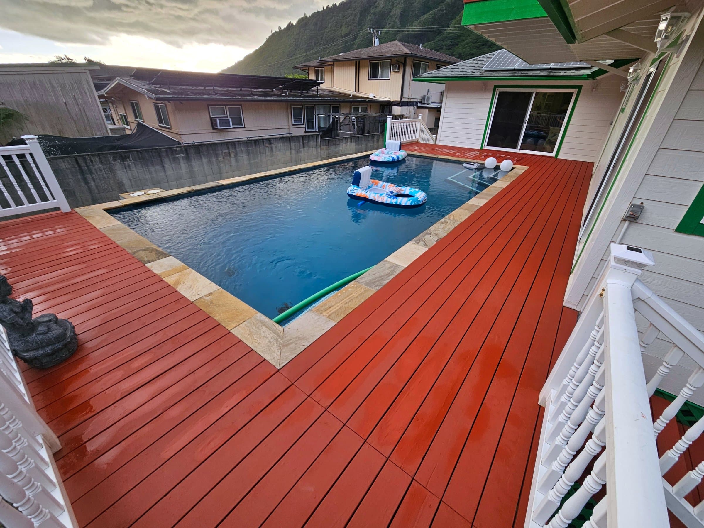 Freshly stained red pool deck with white railings at sunset, Oahu mountains behind